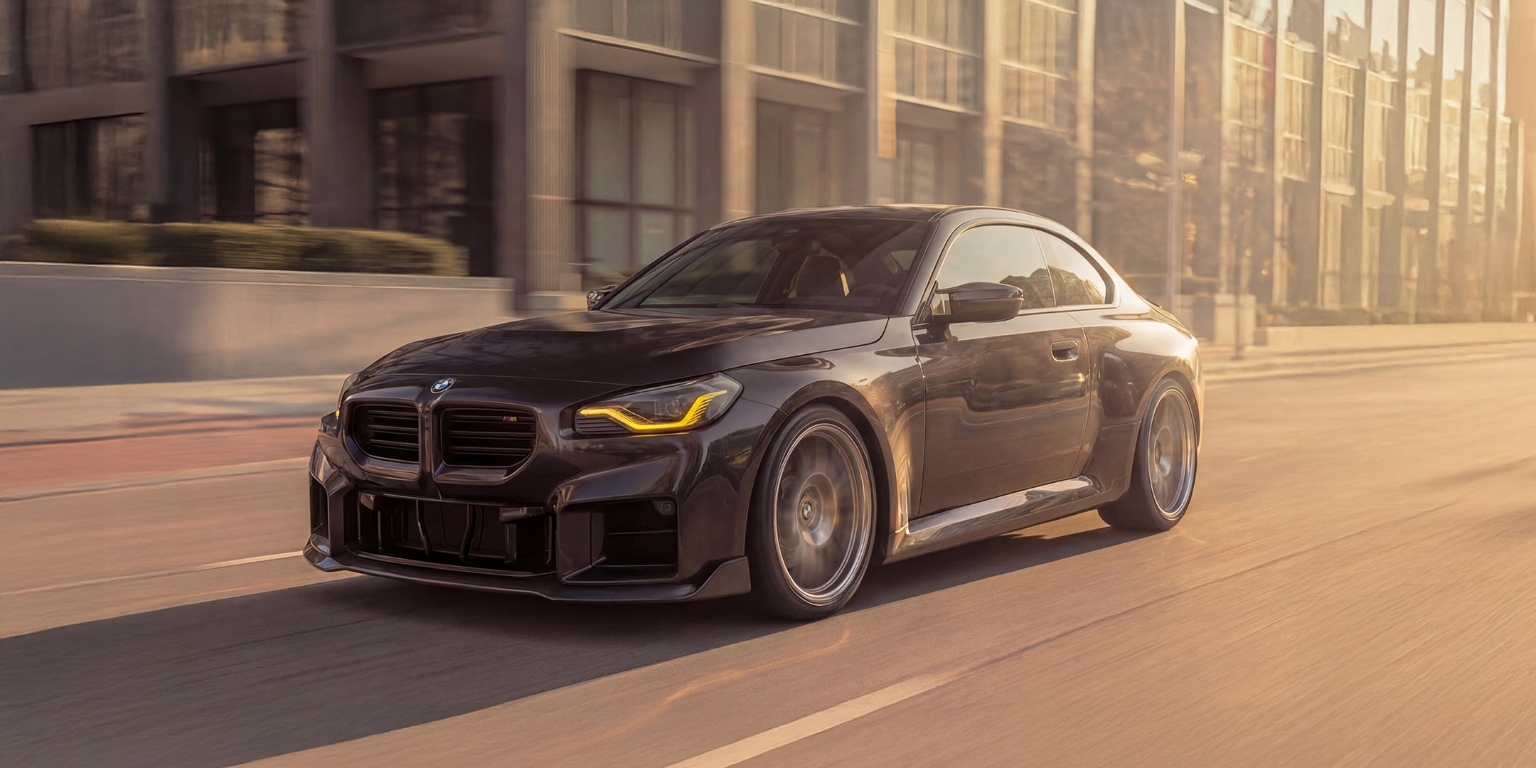 Black WSTN Performance BMW G87 M2 car driving on a road with buildings in the background